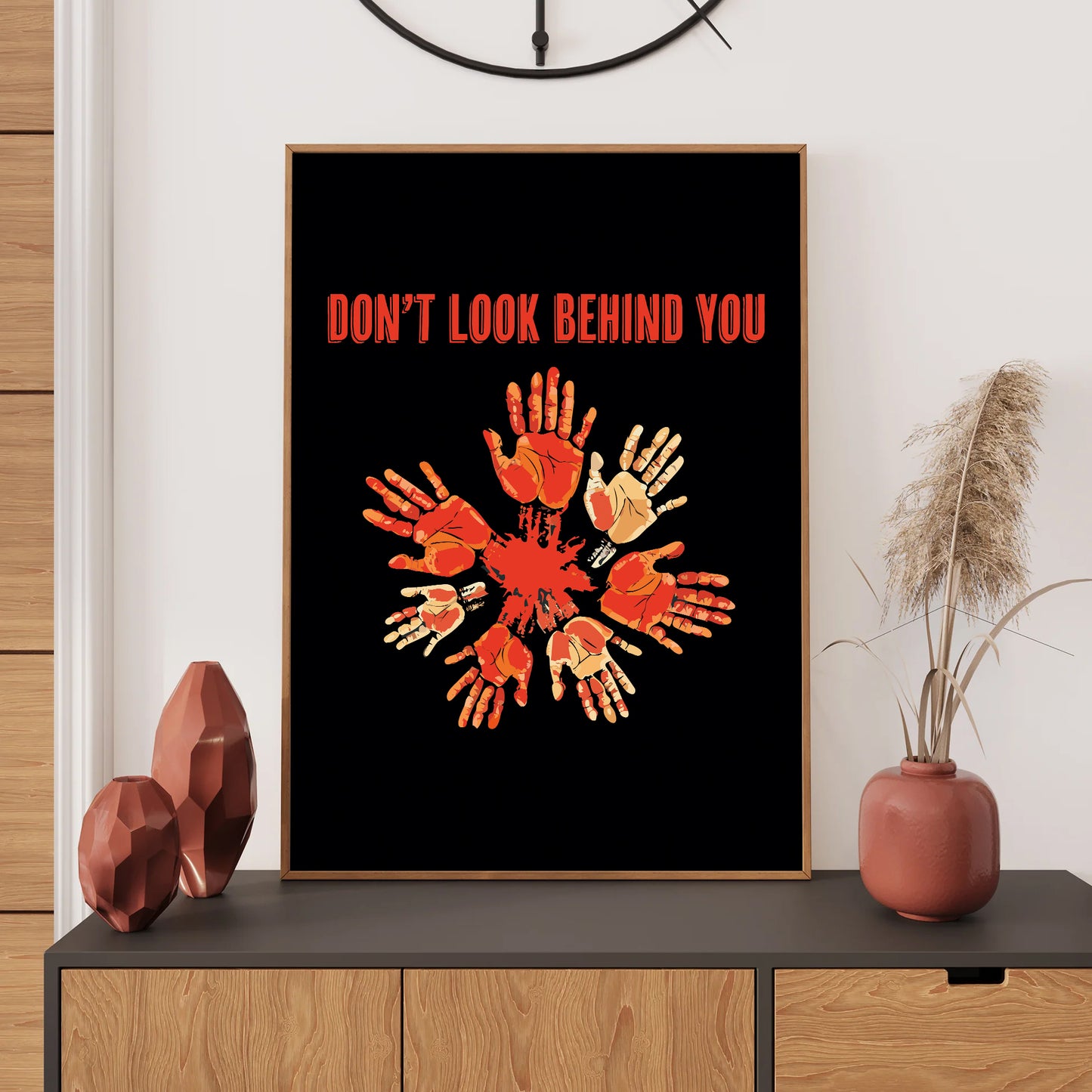 Framed artwork with 'Don't Look Behind You' text and handprints on a black background, displayed on a wooden shelf.