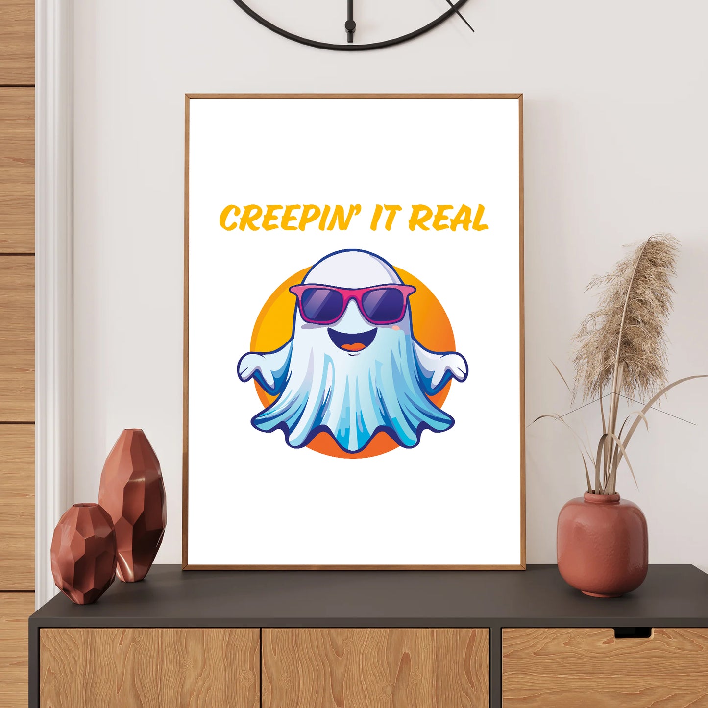 Framed artwork with a ghost wearing sunglasses and 'Creepin' It Real' text on a wall above a console table.
