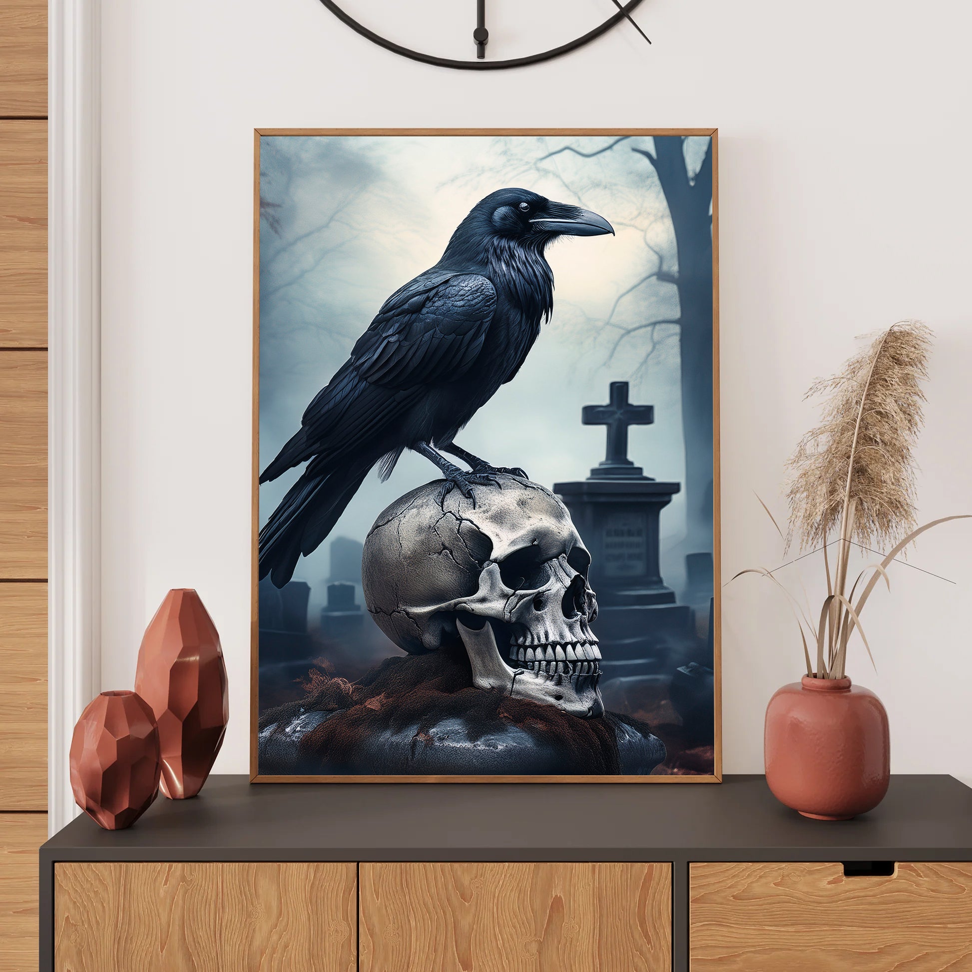 Framed artwork of a crow on a skull with a cemeteriescape, displayed on a wall above a wooden cabinet.