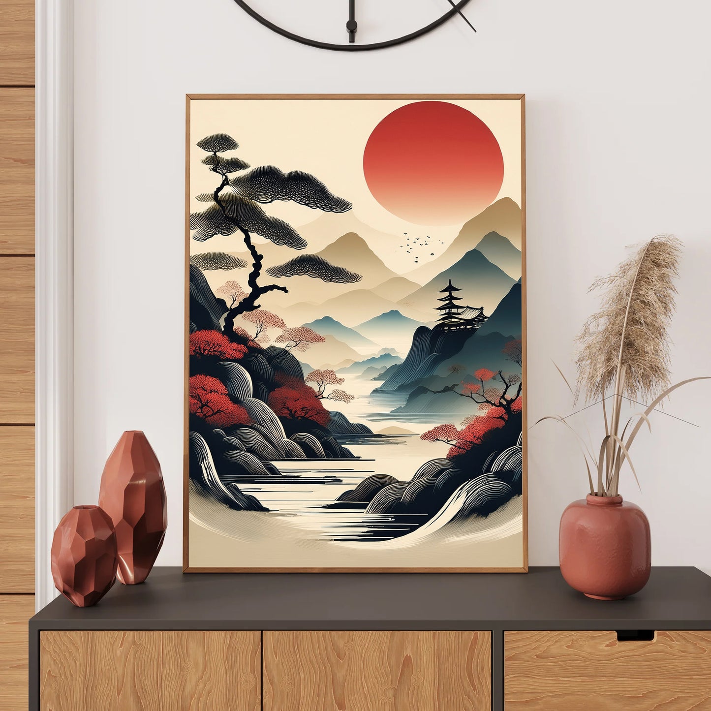 Framed artwork of a Japanese landscape with a red sun, trees, and mountains on a wall above a wooden cabinet.